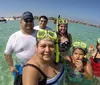A group of six people wearing snorkeling gear takes a selfie while standing in shallow clear waters at a beach