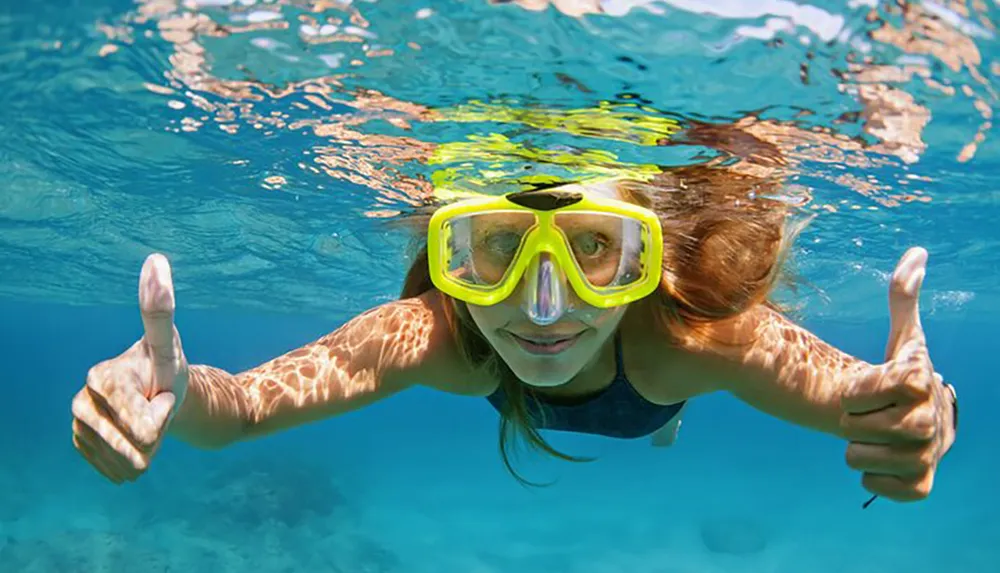 A person is underwater giving two thumbs up while wearing a yellow snorkeling mask