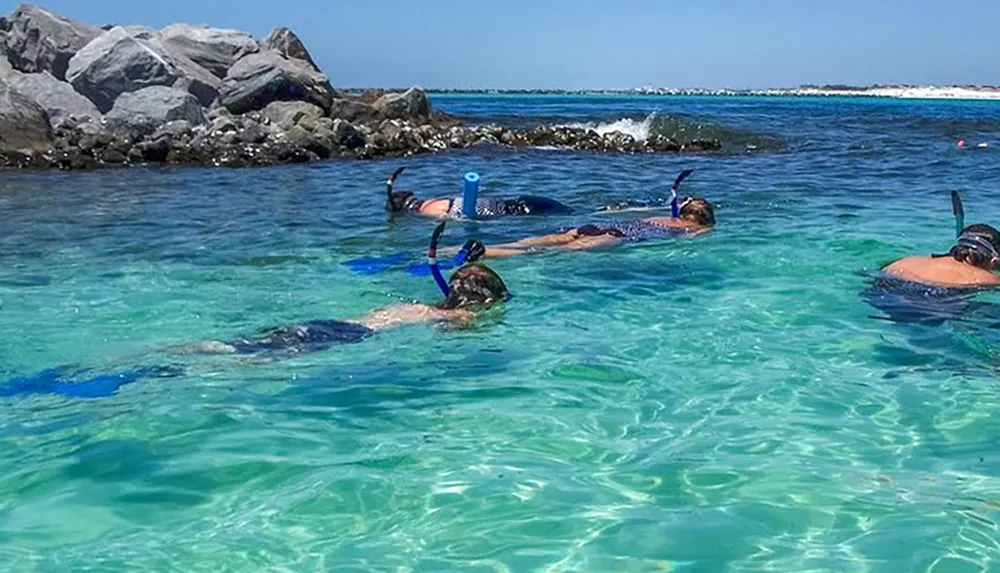 A group of snorkelers is floating in clear turquoise waters near some rocky outcrops likely exploring marine life