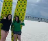 Three smiling people are standing on a sunny beach each with a surfboard ready to enjoy surfing