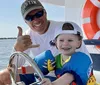 A smiling adult and a young child wearing a life jacket are enjoying time together aboard a boat with the adult giving a thumbs-up gesture
