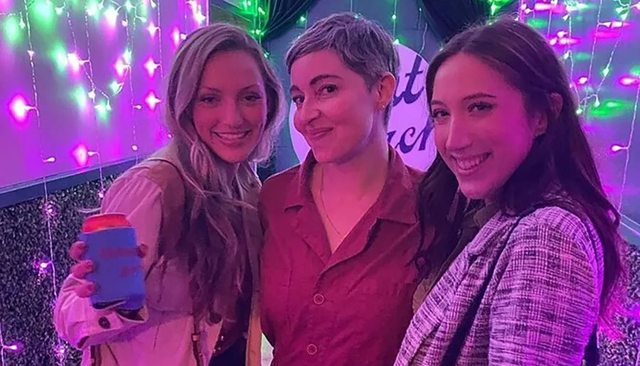 Three smiling people are posing for a photo with colorful lights in the background.