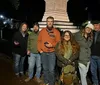 A group of people are gathered outdoors at night some standing and some squatting looking at or using their smartphones