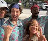 Four cheerful people are posing for a selfie on a sunny day with two individuals wearing matching tropical shirts and everyone exuding a playful and happy vibe