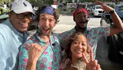 Four cheerful people are posing for a selfie on a sunny day, with two individuals wearing matching tropical shirts and everyone exuding a playful and happy vibe.