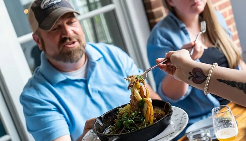 A man appears to be impressed or surprised by a large and loaded forkful of food someone is holding up at a restaurant