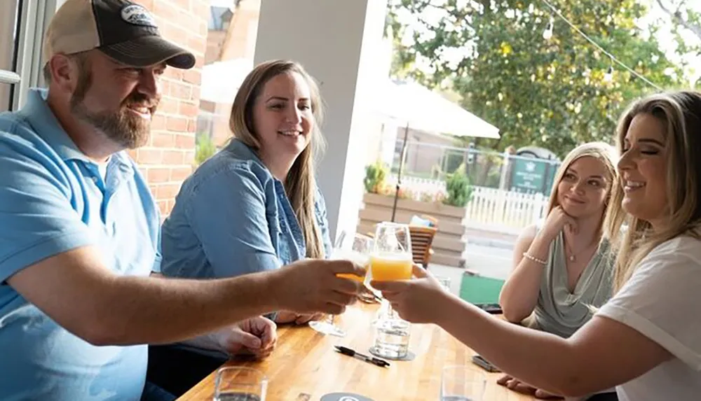 A group of friends are enjoying drinks and each others company at a table with some engaged in a toast