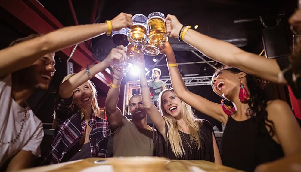 A group of friends is toasting with beer mugs smiling and enjoying a lively atmosphere at a bar or event