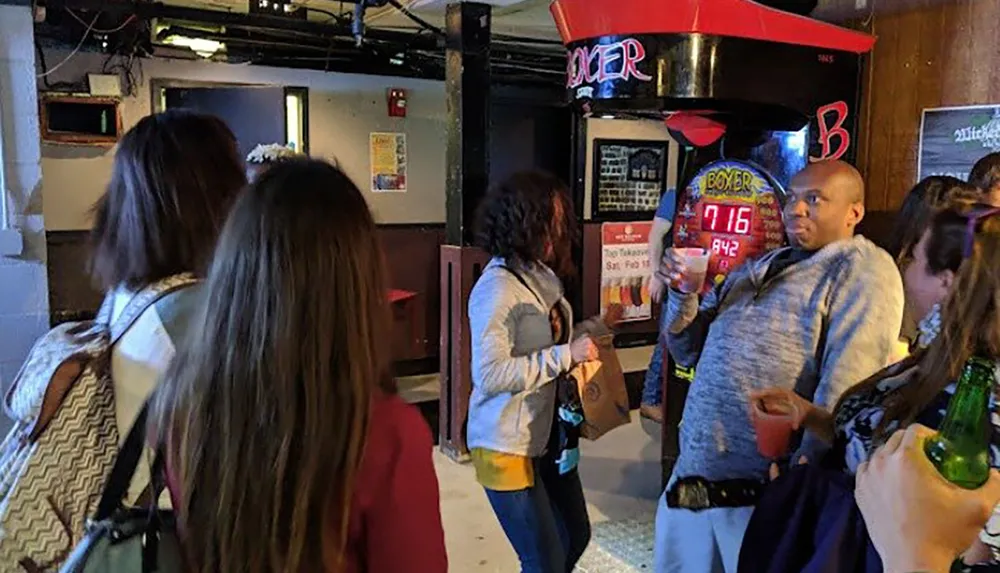 People are socializing in a bar with a punch strength measuring game in the background