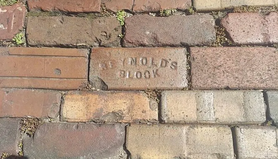 The image shows a weathered brick pavement with one brick stamped with the text REYNOLDS BLOCK.