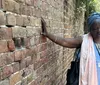 A person is touching an old brick wall with a thoughtful expression on her face
