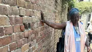 A person is touching an old brick wall with a thoughtful expression on her face.