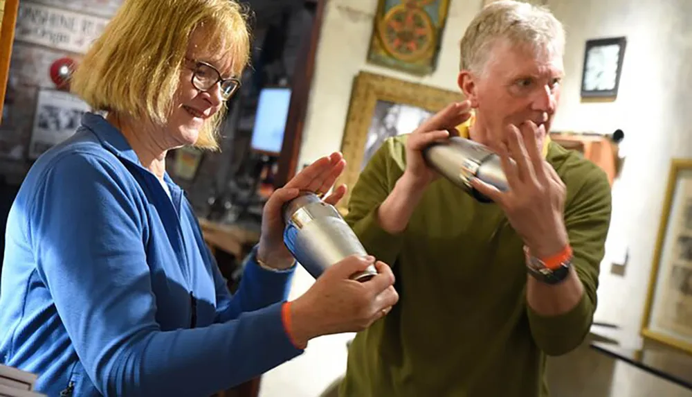 Two people are shaking cocktail shakers with focused expressions in what appears to be a bar or restaurant setting