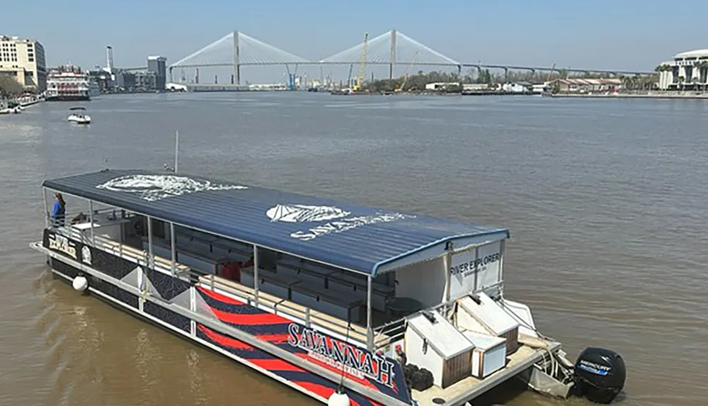 A boat decorated with the word Savannah is cruising on a river with a cable-stayed bridge in the background