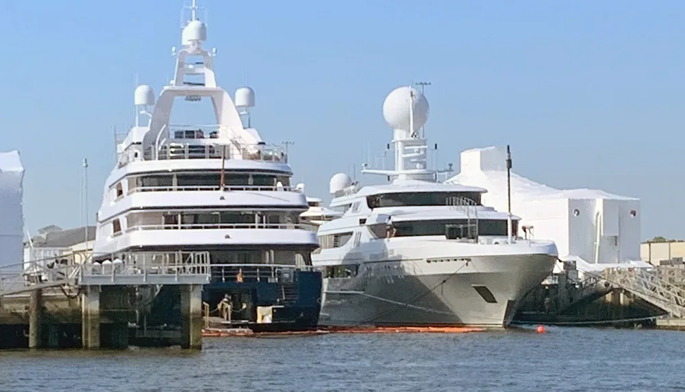 The image shows two large luxurious yachts moored at a dock with several maritime antennas and communication domes on the top decks