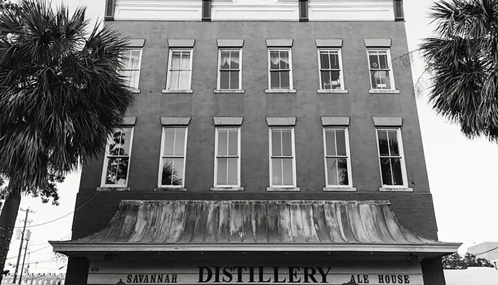 The image shows a black and white photo of a multi-story building with signage indicating Savannah Distillery Ale House flanked by palm trees