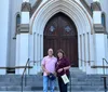 Two people are standing together on the steps in front of the large arched entrance of a church