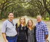 Four adults are posing for a photo on a picturesque tree-lined dirt road
