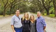 Four adults are posing for a photo on a picturesque tree-lined dirt road.