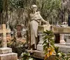 A solemn statue of an angelic figure overlooks a grave in a serene cemetery draped with Spanish moss