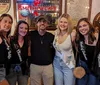 A group of five women wearing sashes with bridal party titles and a man posing together at a bar possibly celebrating a bachelorette party