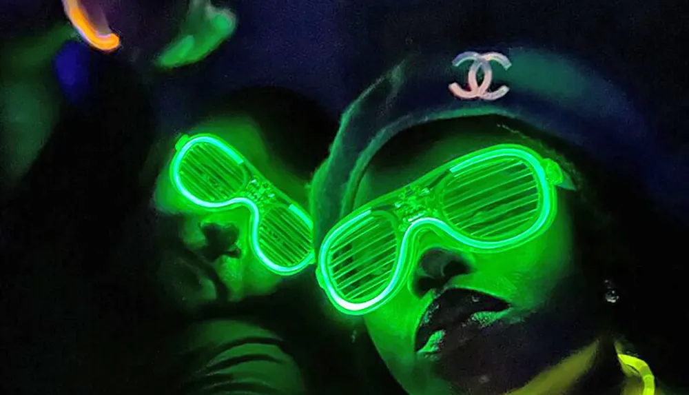 Two people with glowing green light-up glasses are shown in a dimly lit environment giving off a fun and energetic party vibe