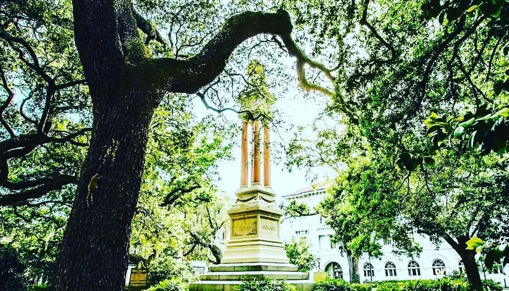 A monument stands amidst lush green trees in a sunlit park setting