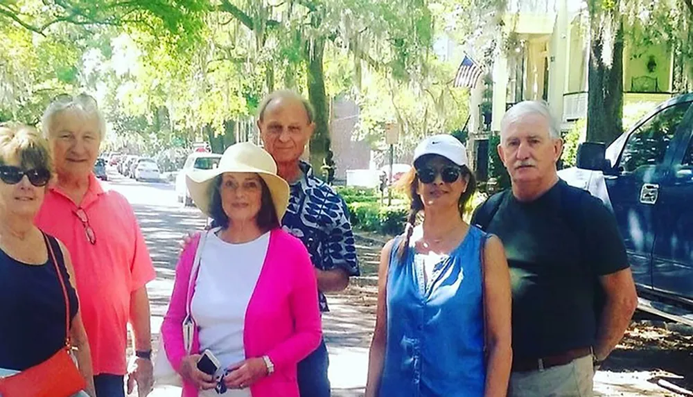 A group of six adults poses for a photo on a tree-lined street exuding a pleasant and casual atmosphere