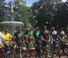 A group of people are posing with their bicycles in front of a fountain on a sunny day