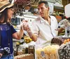 A customer at a market stall is happily purchasing goods from a vendor who is handing a bag of products to her