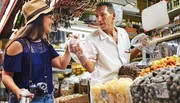 A customer at a market stall is happily purchasing goods from a vendor who is handing a bag of products to her.