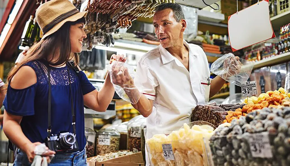 A customer at a market stall is happily purchasing goods from a vendor who is handing a bag of products to her