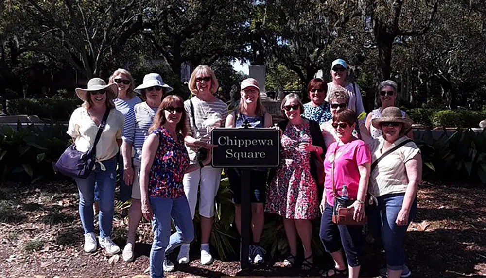 A group of people is posing for a photo next to the Chippewa Square sign in a leafy outdoor setting