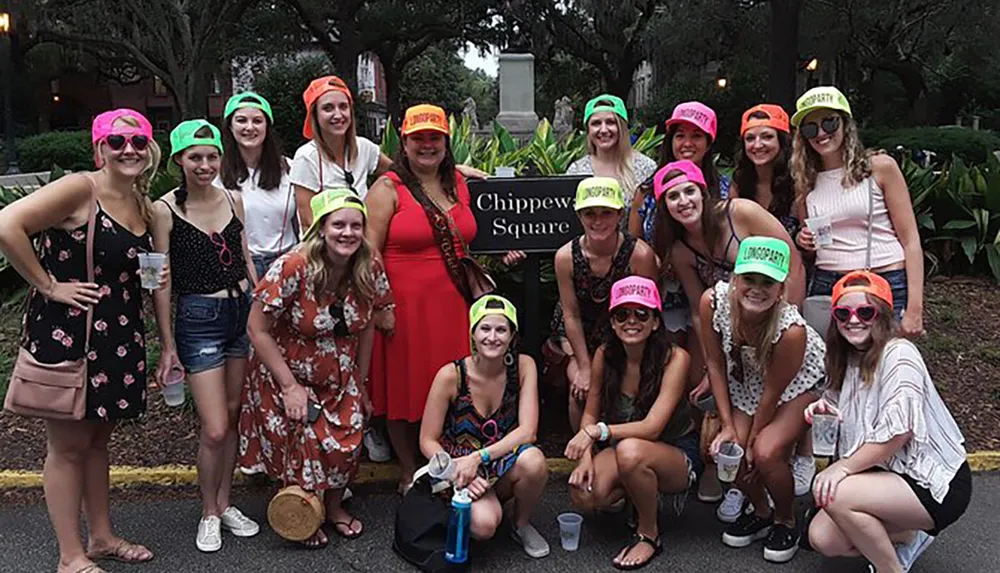 A group of women wearing colorful caps with the text Bachelorette are posing for a photo at Chippewa Square