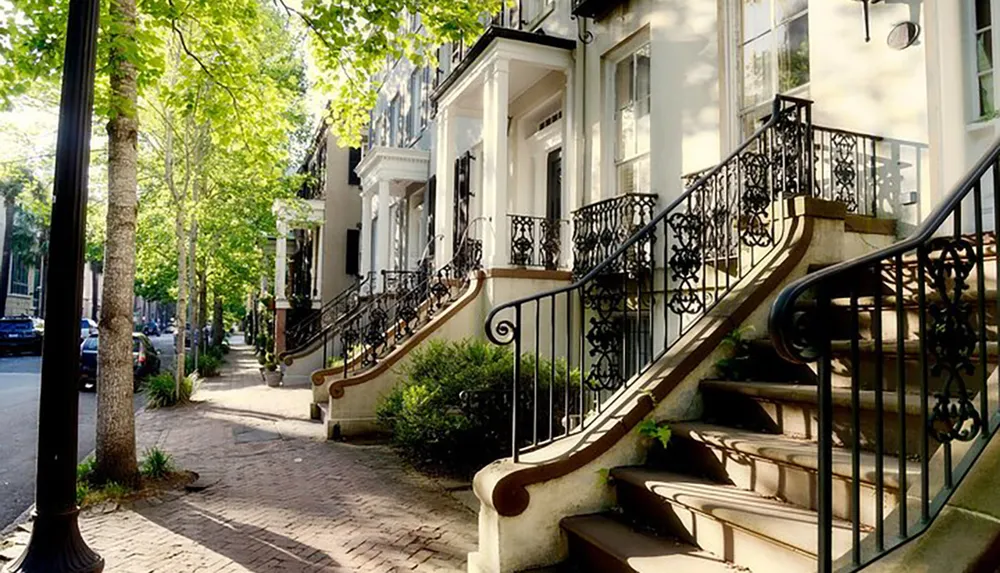 The image shows a charming tree-lined street with elegant townhouses featuring ornate ironwork railings on their staircases