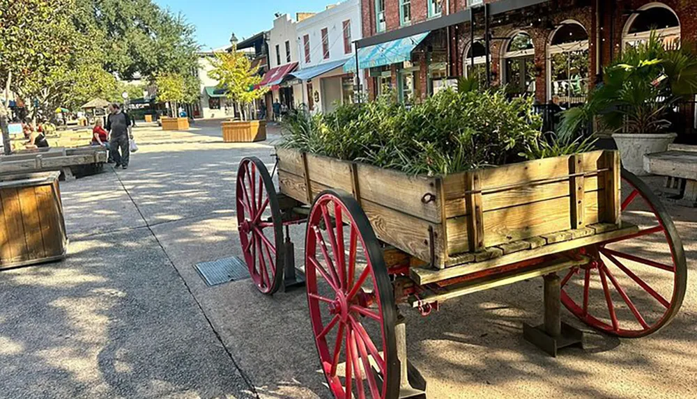 An outdoor pedestrian street is adorned with wooden planters on wheels benches and people strolling with storefronts lining the walkway