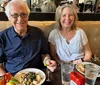 A smiling man and woman are sitting in a booth at a restaurant with plates of food in front of them and drinks on the table