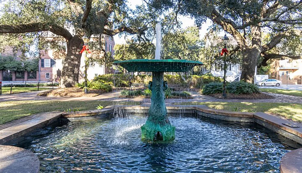 A tranquil fountain sits amid lush greenery and trees adorned with red ribbons suggesting a serene park setting with a hint of festive decoration