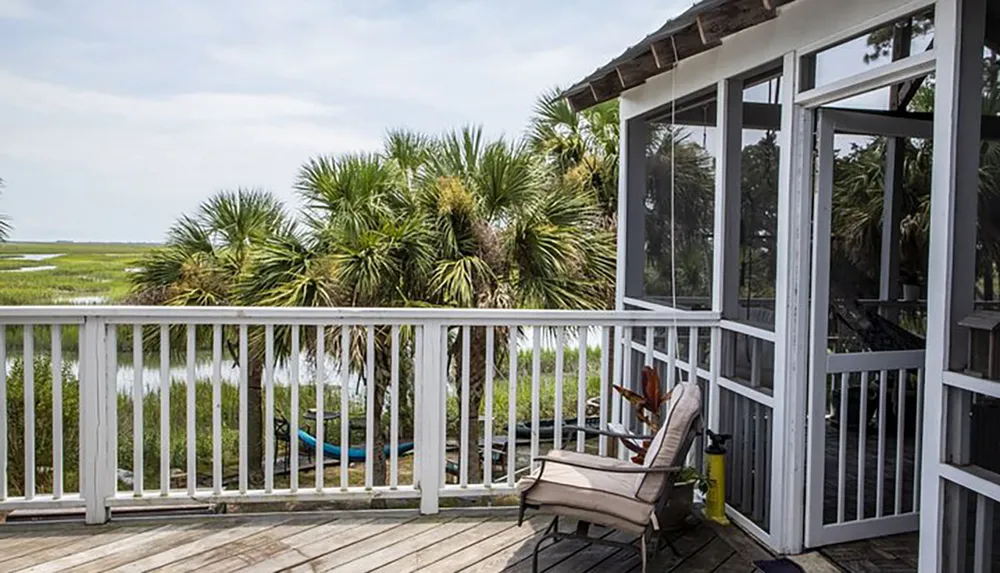 The image shows a tranquil waterfront deck with a lounge chair surrounded by natural scenery and overlooking a calm marshland