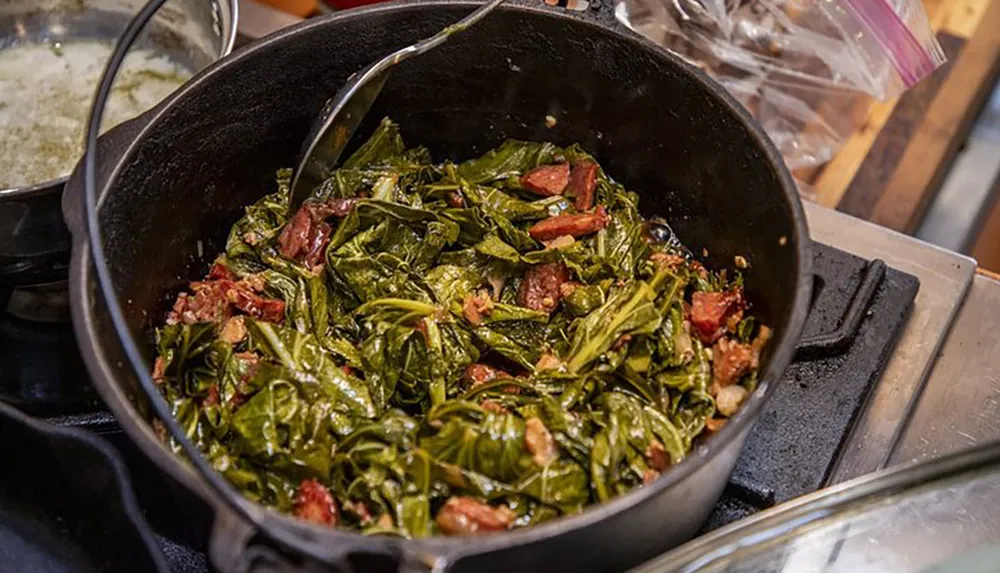 A large cast iron skillet filled with cooked collard greens and chunks of bacon on a stovetop