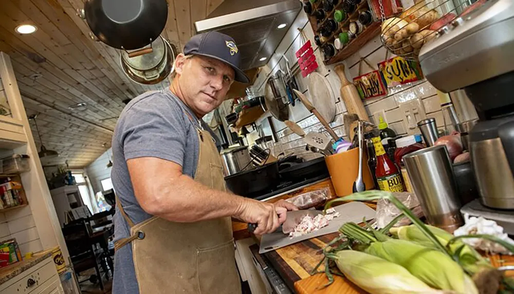 A person in an apron and baseball cap is preparing food in a well-equipped homey kitchen setting