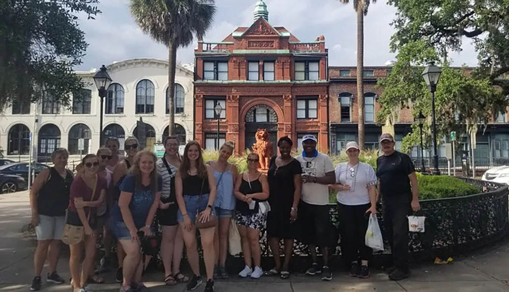 A diverse group of people is posing for a photo in front of a historic-looking building with a distinctive red facade and a lion statue on the rooftop