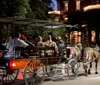 A horse-drawn carriage carrying passengers travels through a dimly-lit urban area at dusk or night