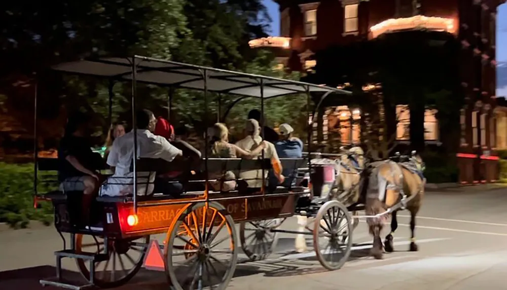 A horse-drawn carriage carrying passengers travels through a dimly-lit urban area at dusk or night