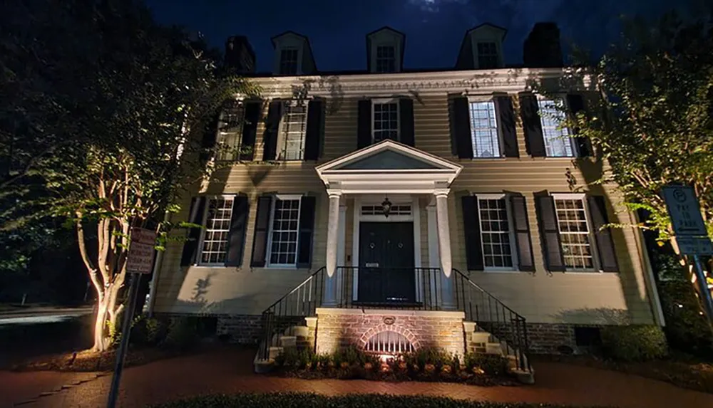 This is an image of a large historic-looking house at night illuminated by external lighting and featuring classic architectural details