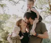 A family is enjoying a sunny day outdoors with the parents holding their young childrens hands and two dogs walking alongside