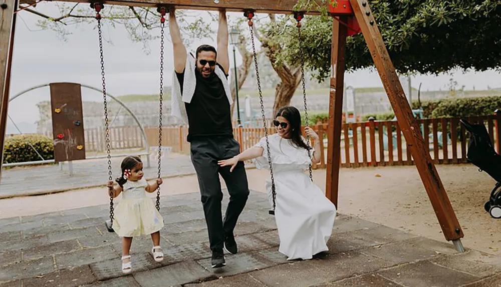 A family with two adults and a child enjoys time together at a swing set in a park