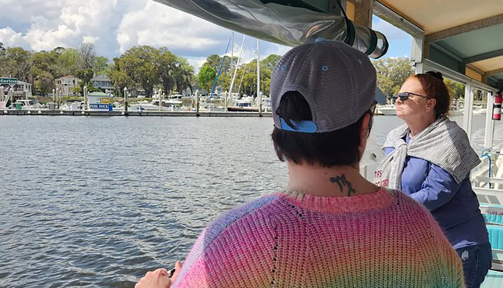 Two people are enjoying a boat ride with a scenic view of a marina with moored boats and waterfront houses