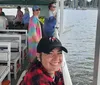 A smiling person in a black cap is posing for a photo on a boat with several other passengers enjoying the ride in the background