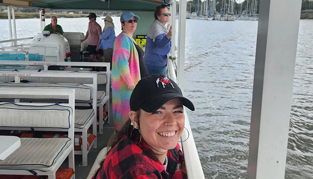 A smiling person in a black cap is posing for a photo on a boat with several other passengers enjoying the ride in the background